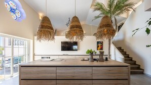 A modern kitchen with a large island, pendant lights, and a TV above it. - Bedroom in a Villa, Budens (Vila do Bispo)
