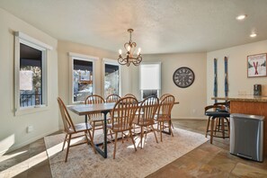 A dining area with a wooden table and chairs, a chandelier, and a kitchen area with a refrigerator and bar counter. - Walk to Main Street & Ski Access (Park City)