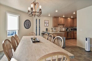 A dining area with a wooden table and chairs, a chandelier, a clock, and a kitchen with wooden cabinets and appliances. - Walk to Main Street & Ski Access (Park City)