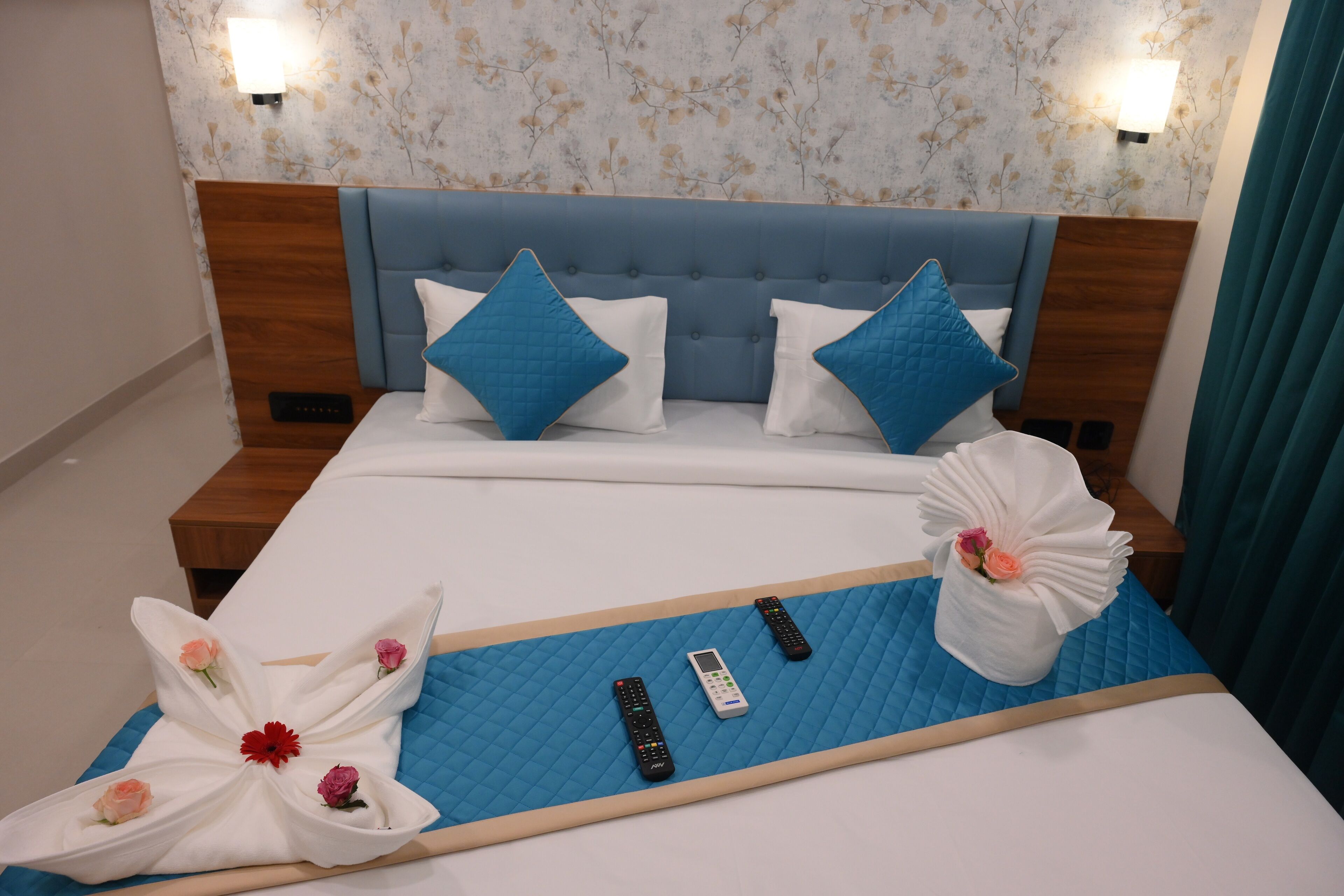 Habitación de hotel con cama, mesita de noche, lámpara de pared y papel tapiz con motivos florales.