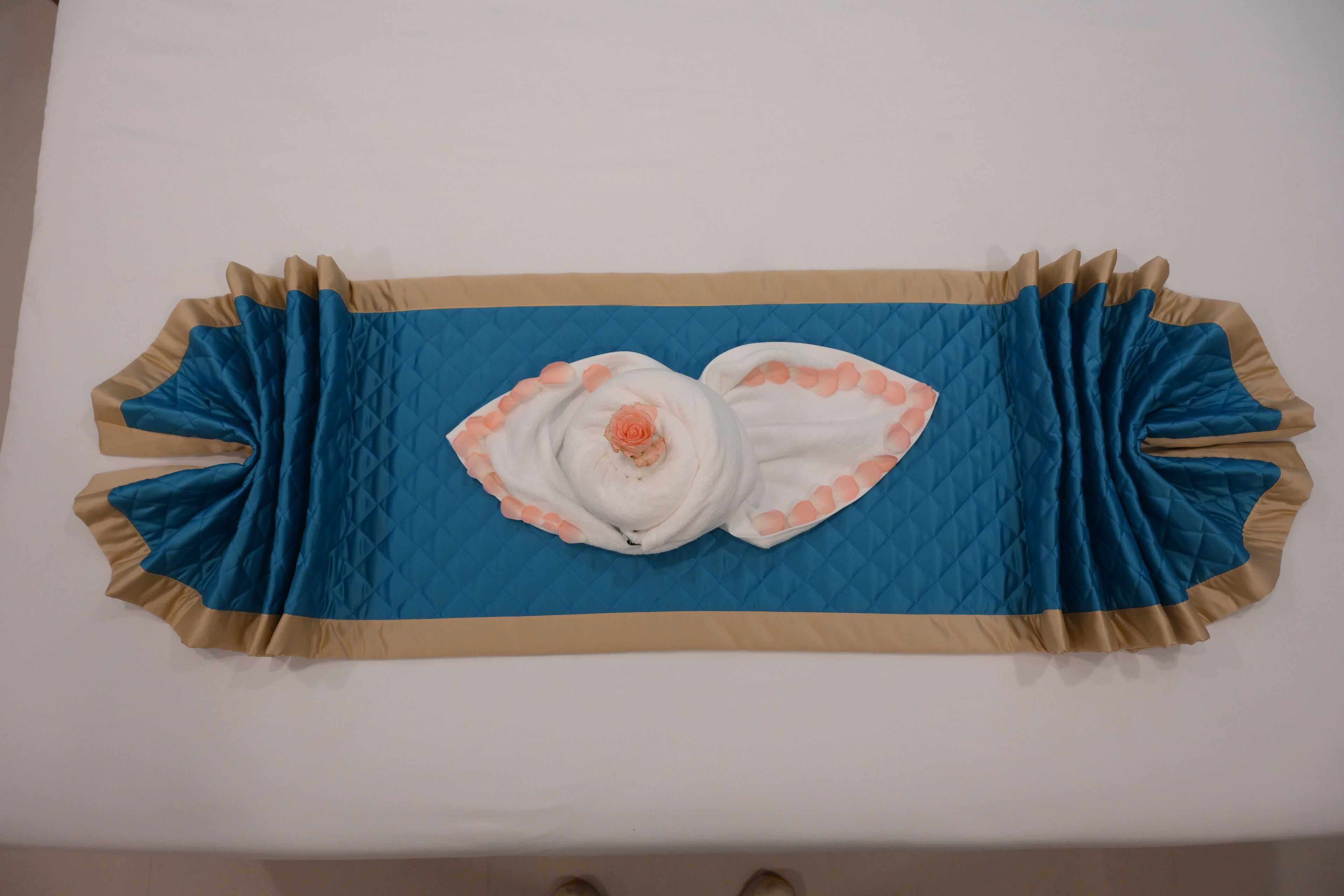 A bed with a blue quilted cover and a white pillow with a peach-colored design.
