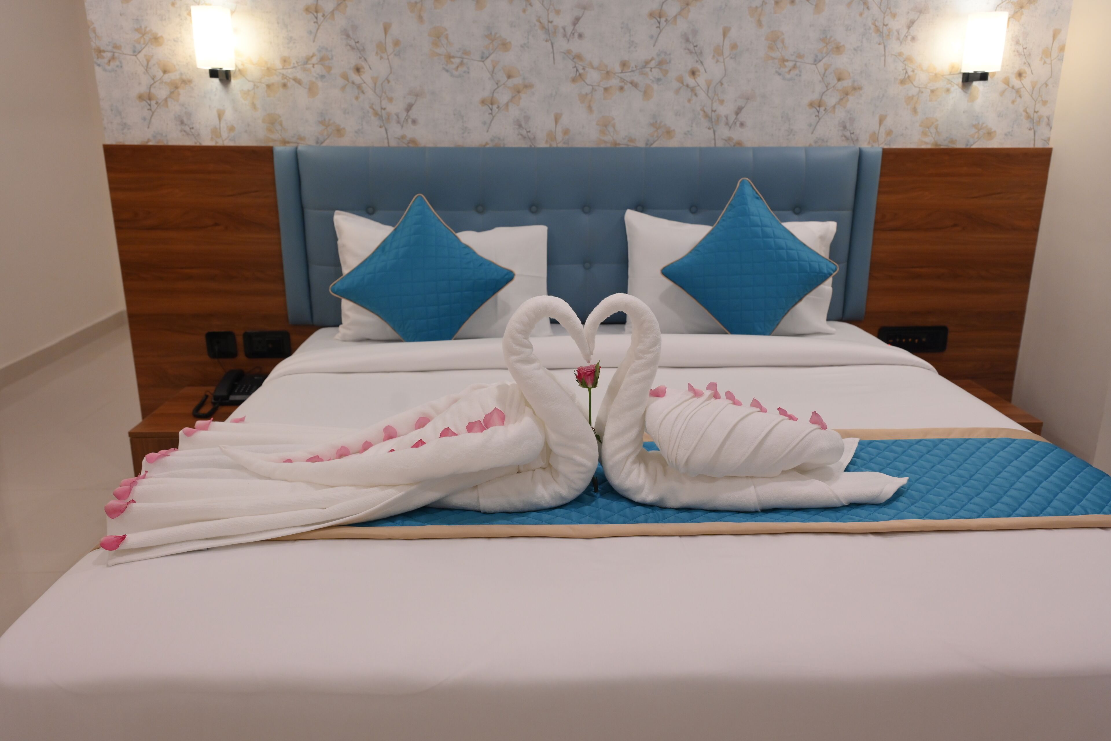 Un lit bien fait, avec une tête de lit bleue, deux oreillers bleus et une serviette décorative en forme de cygne.