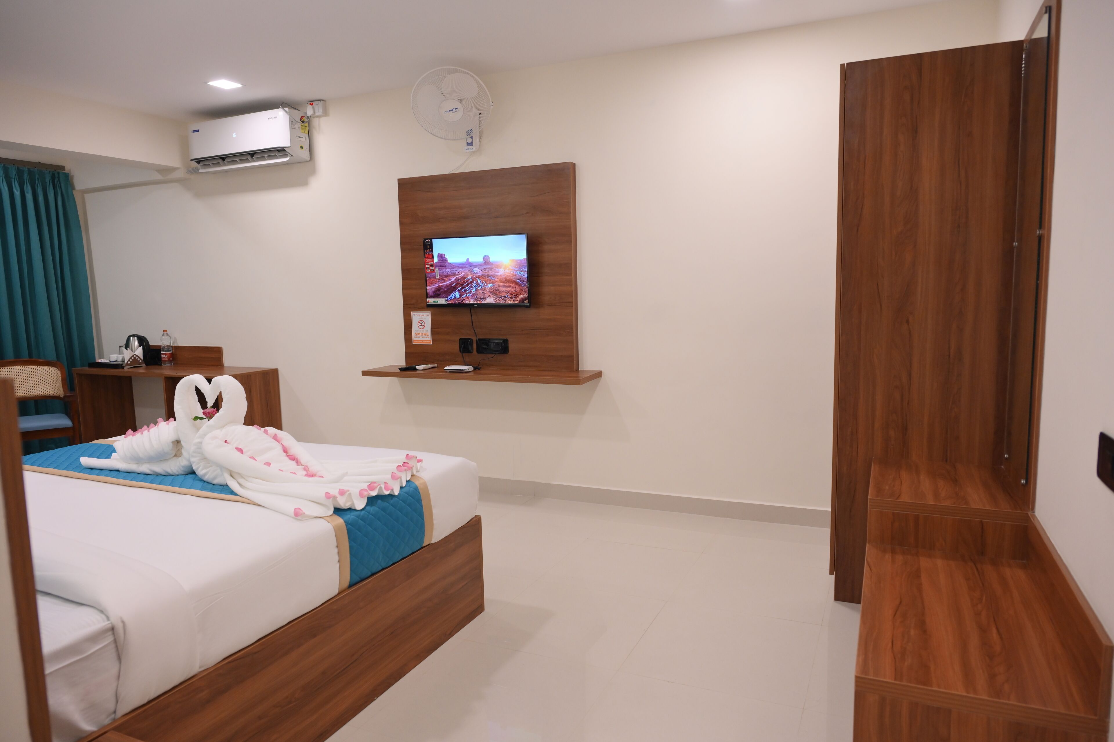 A hotel room with a bed, a TV mounted on the wall, an air conditioning unit, and a wooden wardrobe.