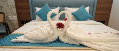Un lit recouvert d’une courtepointe bleue matelassée, d’une couverture blanche et de deux serviettes en forme de cygne, chacune ornée d’une fleur rouge au centre.