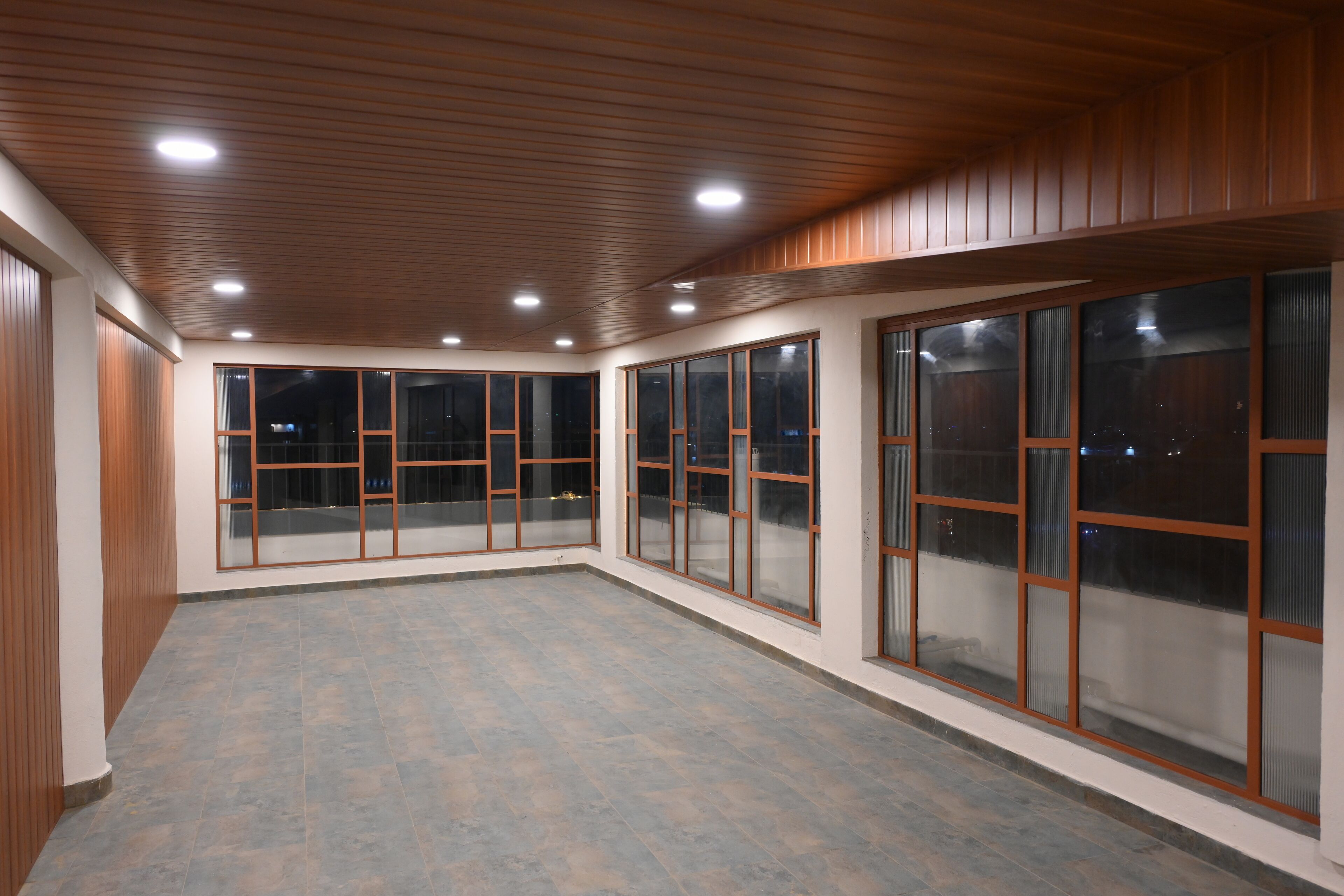 Une pièce spacieuse dotée de grandes fenêtres, de panneaux de plafond en bois et d’un sol carrelé.