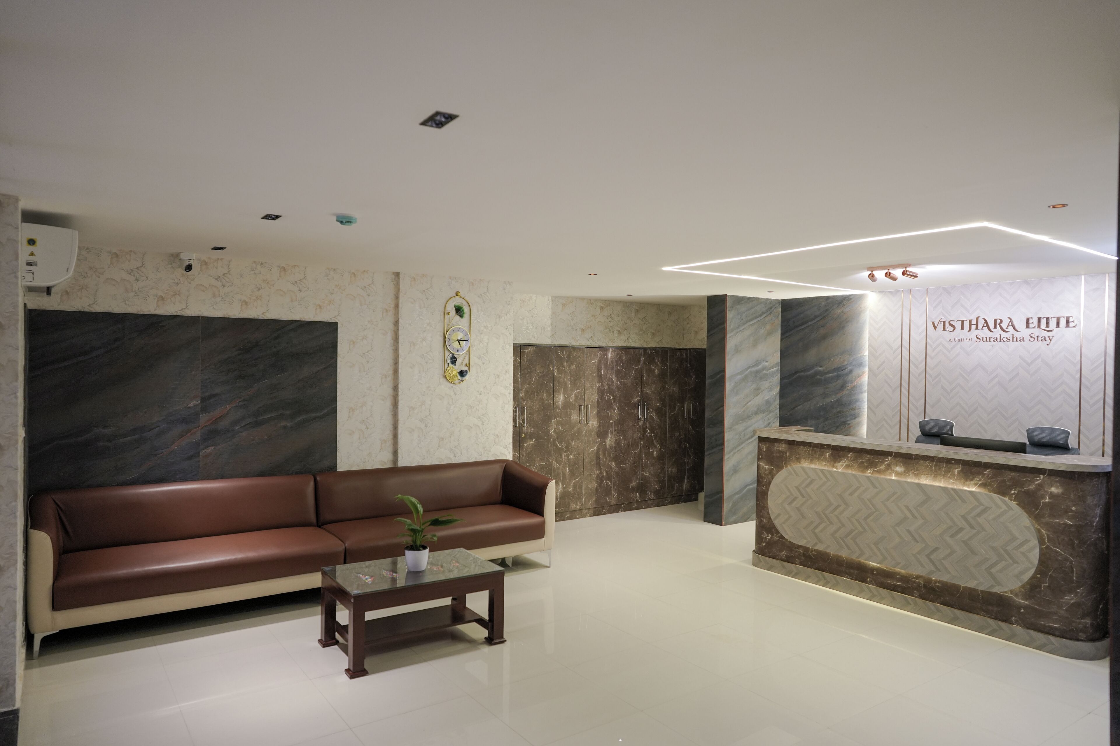 A reception area with a brown leather sofa, a reception desk, and a potted plant.