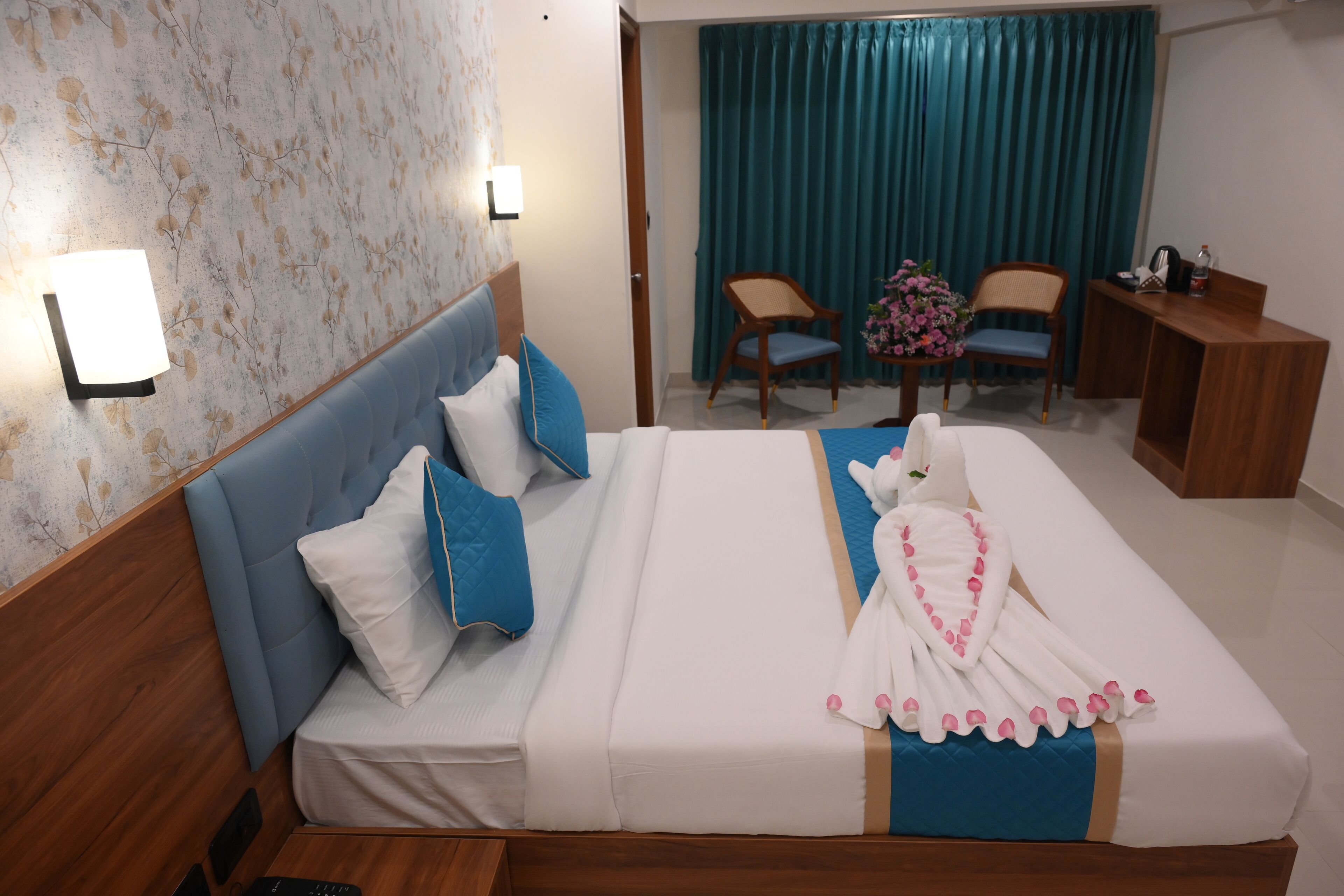 A hotel room with a bed, two chairs, a desk, and a window with curtains.