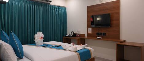 A hotel room with a bed, a TV mounted on the wall, a bedside table, and a ceiling fan.