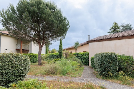 A pathway leading to a building with a tiled roof, surrounded by well-maintained hedges and a large evergreen tree.. 'Villa Léonidas' – Peaceful Stay in Léon, Near Lake and Ocean