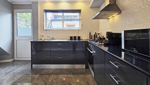 A modern kitchen with a large island, black cabinetry, and a stainless steel range hood. - Casa da Maré Azul (São Roque)