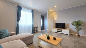 A modern living room with a sofa, a coffee table, a TV, and a potted plant. - Casa da Maré Azul (São Roque)