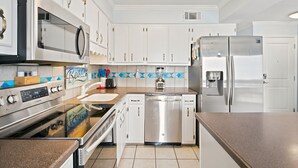 Una cocina moderna con electrodomésticos de acero inoxidable, armarios blancos y un salpicadero azul y blanco.