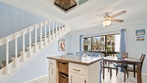 Una cocina con una isla central, muebles blancos y un comedor con mesa y sillas.