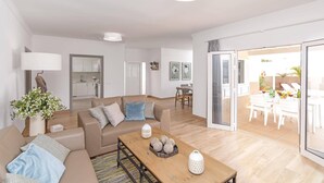 A modern living room with a sofa, coffee table, and a dining area with chairs and a table. - Villa Olivina 1 by Villa Plus (Tías)