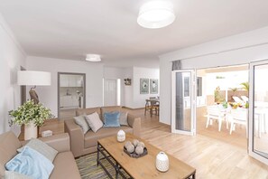 A modern living room with a sofa, coffee table, and a dining area with chairs and a table. - Villa Olivina 1 by Villa Plus (Tías)