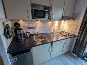 A compact kitchen with a microwave, stove, sink, and dishwasher. - Vacation home Sommerflieder (De Cocksdorp)