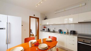 A modern kitchen with white cabinets, a built-in oven, and a dining area with a wooden table and chairs. - Villa Sapri by Villa Plus (Playa Blanca)