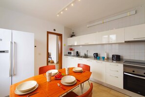 Eine moderne Küche mit weißen Schränken, einem eingebauten Ofen und einem Essbereich mit einem Holztisch und Stühlen.