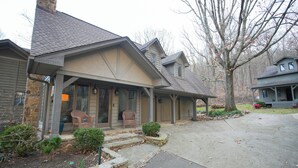 A two-story house with a stone chimney, a covered porch with chairs, and a well-maintained front yard. - Dug Hill Home with Patio, Pond & Fire Pit! (Brownsboro)