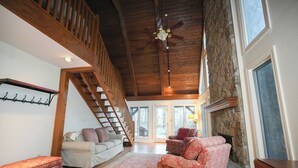 A spacious living room with a high ceiling, a wooden staircase, and a stone fireplace. - Dug Hill Home with Patio, Pond & Fire Pit! (Brownsboro)