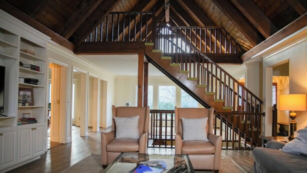 A spacious living room with a high wooden ceiling, a staircase, leather armchairs, and a glass coffee table. - Dug Hill Home with Patio, Pond & Fire Pit! (Brownsboro)