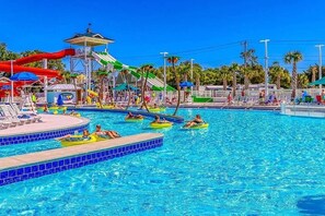 Une piscine avec plusieurs couloirs de nage, un toboggan aquatique et des espaces de détente avec des parasols.
