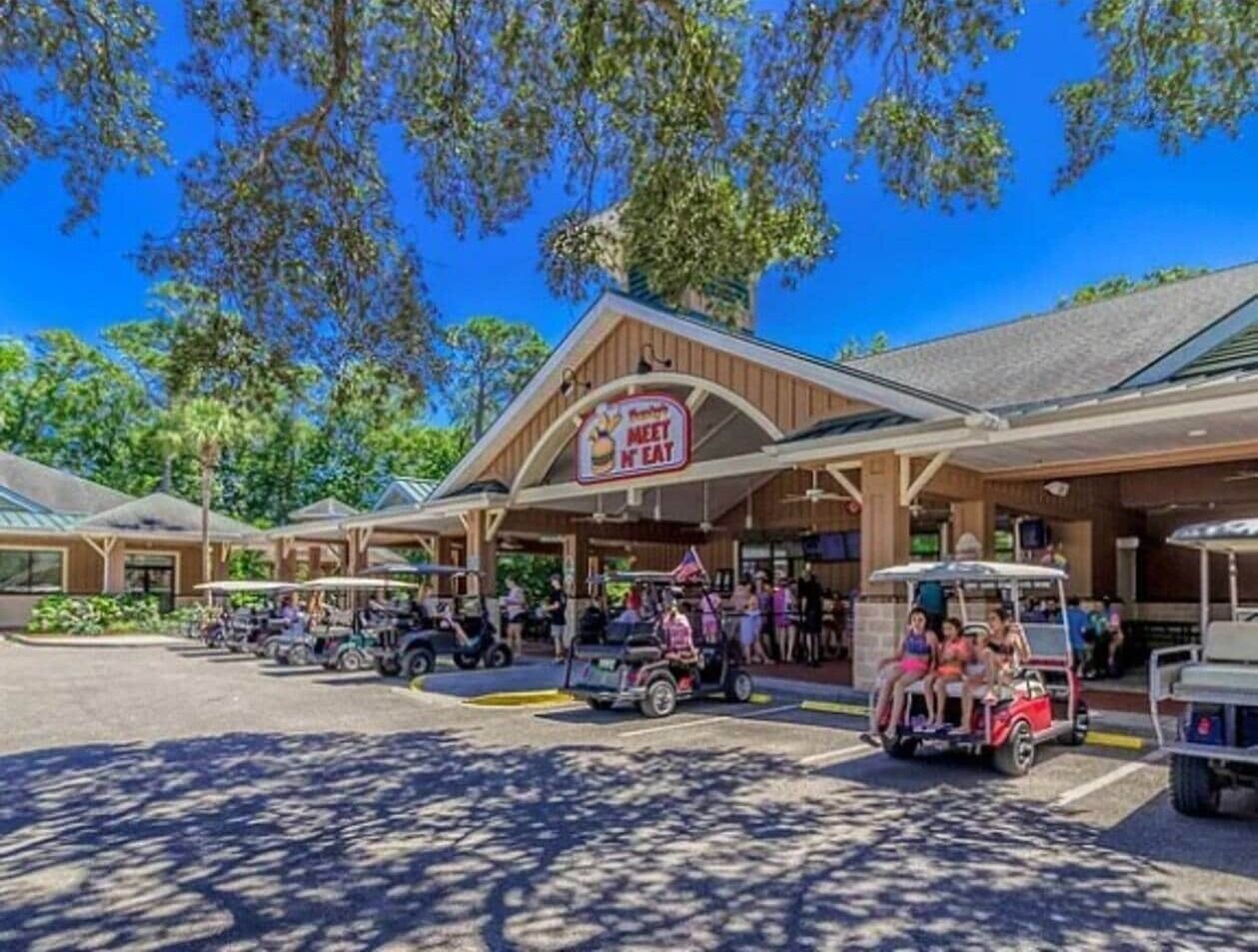 A restaurant with a 'Meet N Eat' sign, outdoor seating, and golf carts.