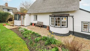 Ein traditionelles Reetdachhaus mit kleinem Garten und einer Bank.