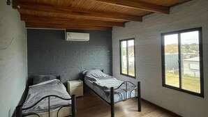 A room with two single beds, a small bedside table, a window, and a wooden ceiling.
