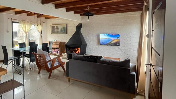 A living room with a fireplace, a TV mounted on the wall, and a dining area with chairs and a table.