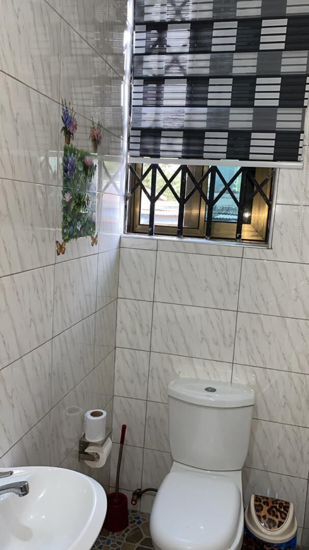 Un baño con inodoro, lavamanos y ventana con persiana a cuadros.