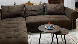 A living room with a sectional sofa, a round coffee table, a hanging light fixture, and a framed picture on the wall. - NickJaak Courtyard Rooms (Accra)