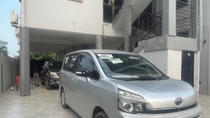 Une voiture argentée est garée dans un parking couvert, avec un immeuble à plusieurs étages en arrière-plan.