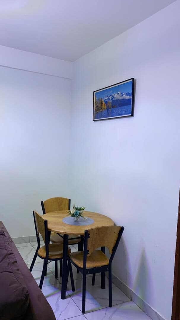 A small dining area with a wooden table and chairs, a painting on the wall, and a brown sofa.