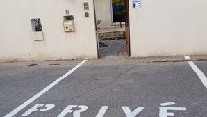 Een parkeerplaats met 'PRIVE' op de grond geschilderd, een gebouw-ingang en een bord waarop 'ATTENTION CHIEN' staat.