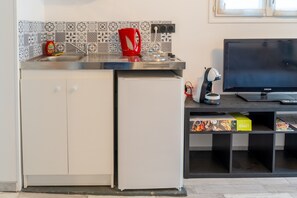 A compact kitchen with a refrigerator, a sink, a kettle, and a television.