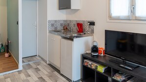 Een kleine keuken met een magnetron, waterkoker en koffiezetapparaat, een televisie op een standaard en een kleine koelkast.