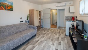 Een moderne woonkamer met een gestreept bankje, een houten kast en een keukenhoek met een koelkast, magnetron en koffieapparaat.