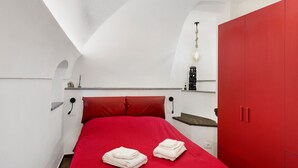 Un dormitorio con una colcha roja, un armario rojo y un techo blanco.