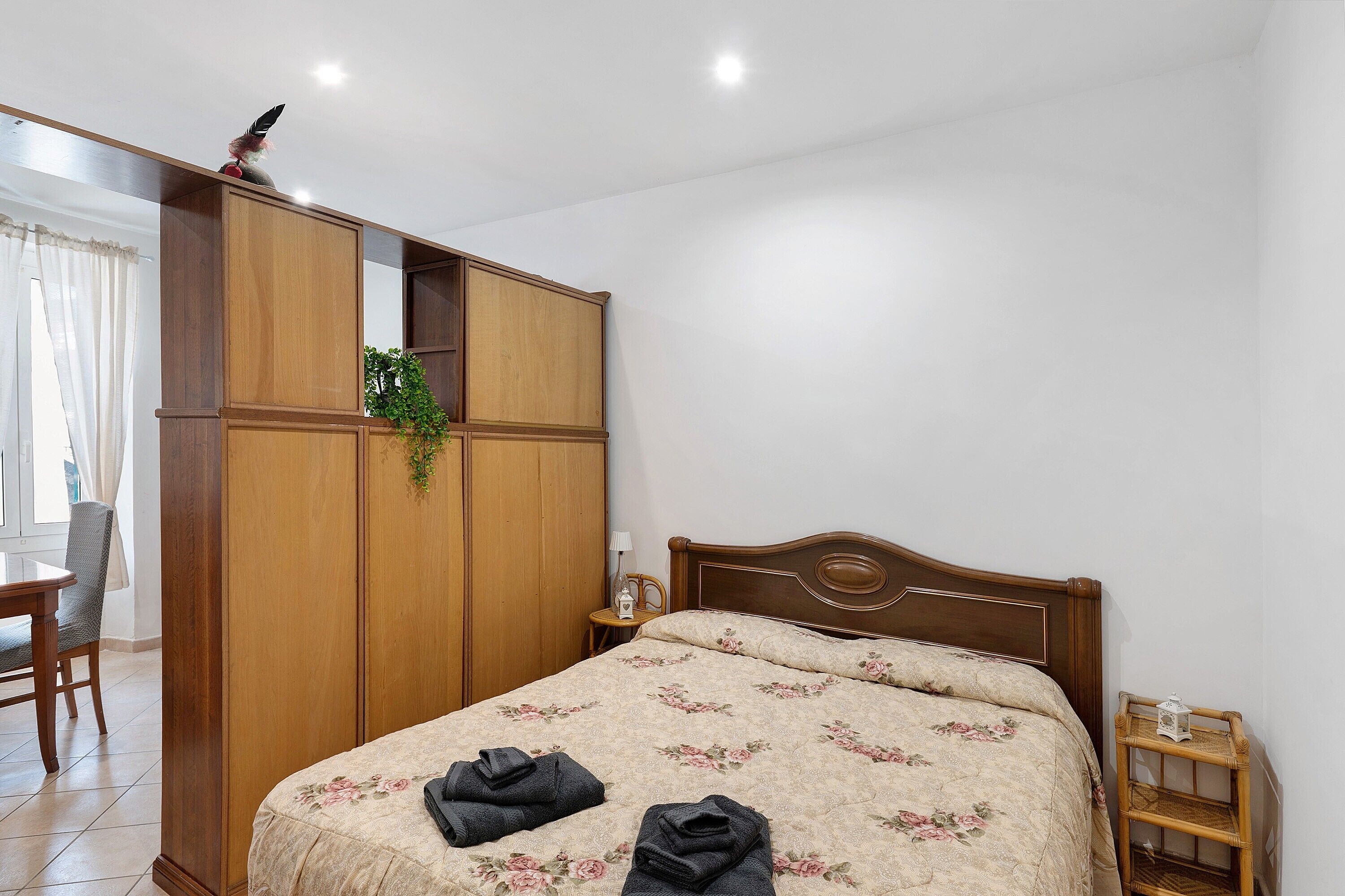 Une chambre à coucher avec un lit, une armoire en bois, une petite table avec une lampe et une chaise.
