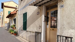 Une rue étroite bordée d’immeubles, une porte avec un numéro, et des plantes en pot.