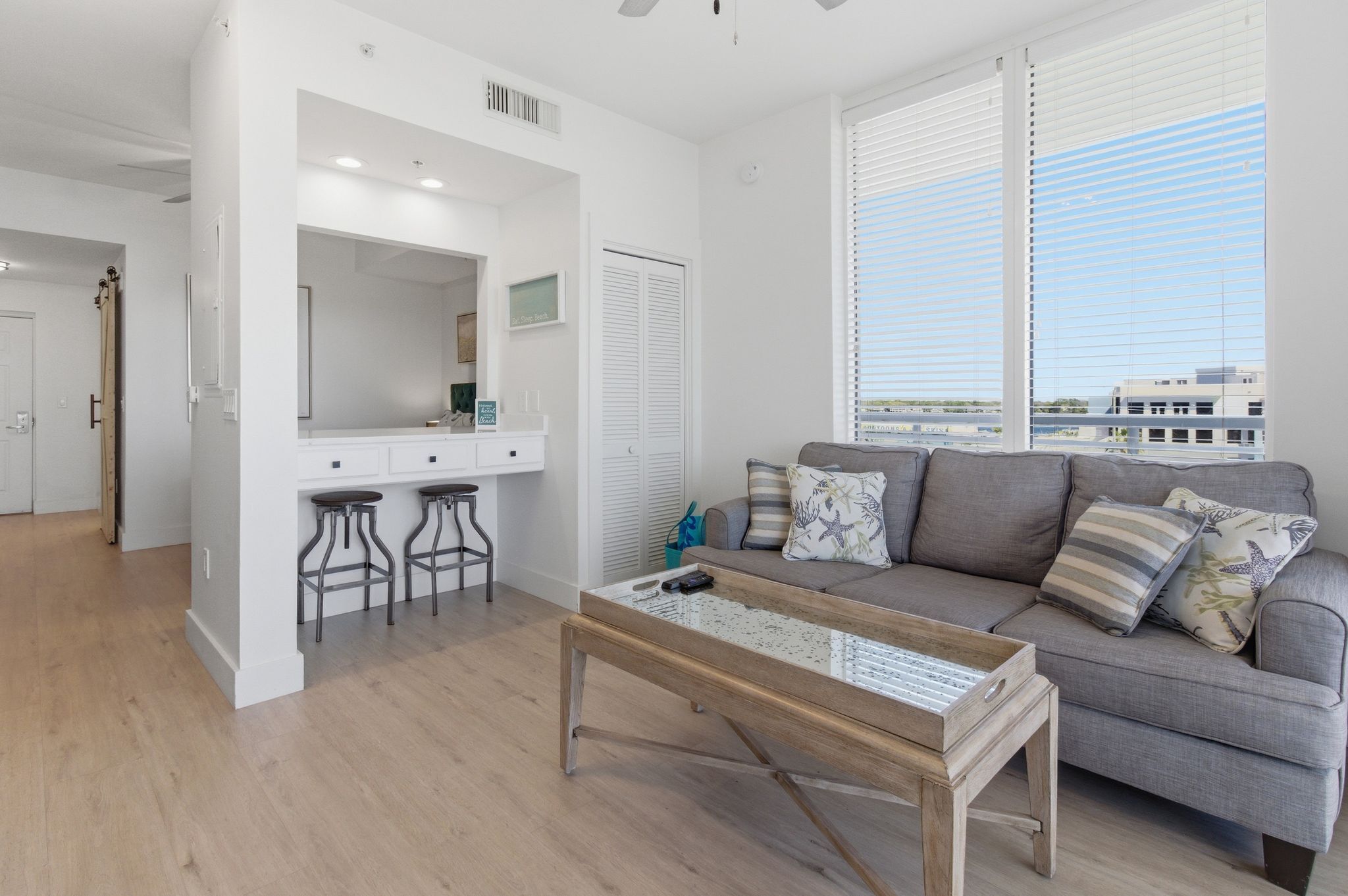 A modern living room with a grey sofa, a coffee table, and a large window with blinds.