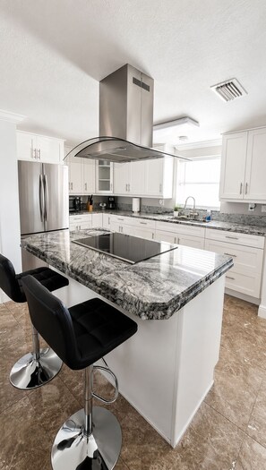 A modern kitchen with white cabinetry, a granite countertop island, and stainless steel appliances. - CASA KAMPA offers you a heated pool with Jacuzzi at no additional cost. (Tampa)