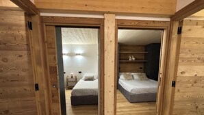Quarto com estrutura de madeira, duas camas, mesa de cabeceira e prateleira com objetos decorativos.