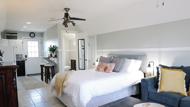 A bedroom with a large bed, a dark blue sofa, a coffee table, and a ceiling fan. - Pine Ridge Getaway (Fort Payne)