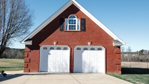 A two-story brick building with a gabled roof and a central arched window. It features two garage doors and a small porch area. - Pine Ridge Getaway (Fort Payne)