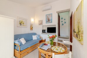 A room with a blue sofa, a dining table with chairs, a vase with flowers, and artwork on the walls.