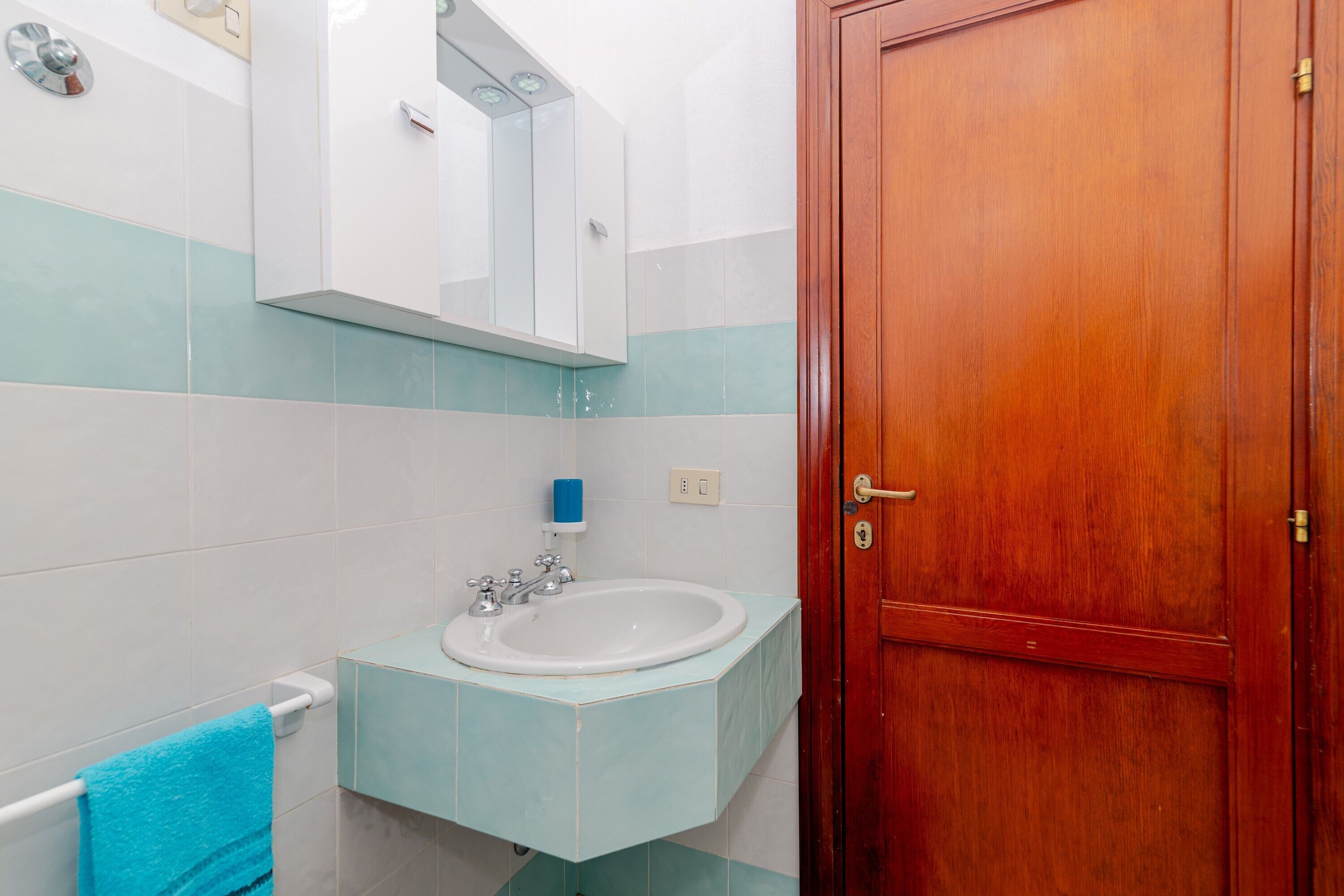 Un baño con un lavamanos blanco, una toalla azul y una puerta de madera.