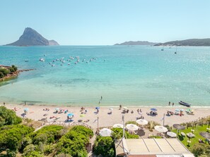 Ein Strand mit klarem türkisblauem Wasser, Booten und Sonnenschirmen.