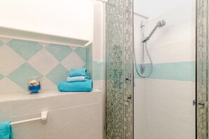 Ein Badezimmer mit Dusche, einer Glasvase mit einem Handtuch und einer gefliesten Wand.